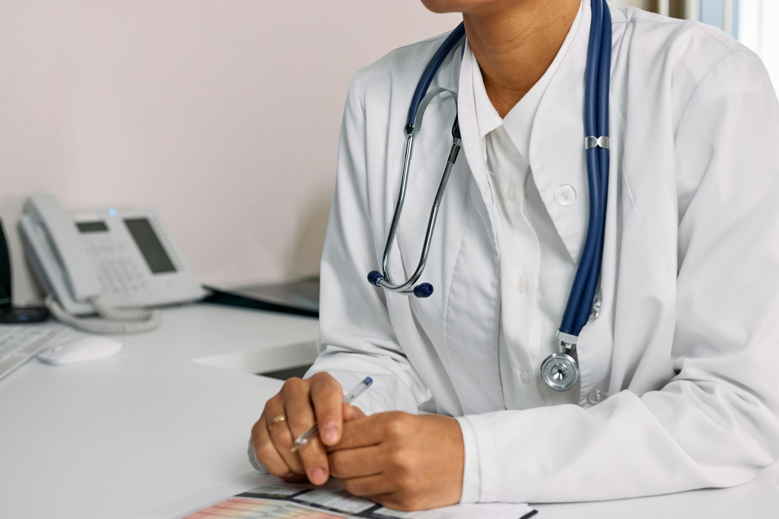 Doctor with stethoscope and white coat seated at a clinic desk.
